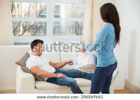 Woman Holding Laundry Basket Looking At Man Using Remote Control