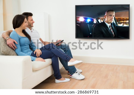 Happy Young Couple In Livingroom Sitting On Couch Watching Movie