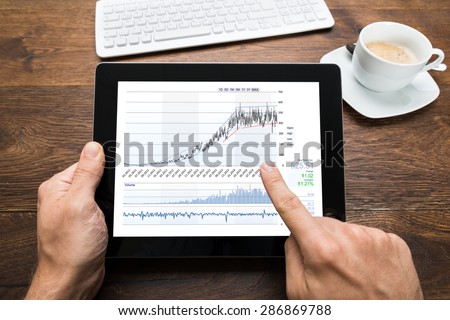 Close-up Of Person Analyzing Graph On Digital Tablet At Desk