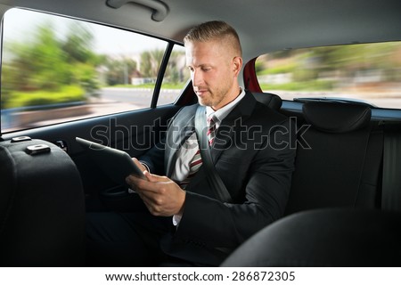 Portrait Of A Businessman Using Digital Tablet While Travelling In A Car
