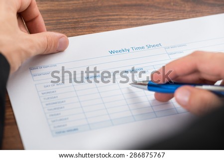Close-up Of Person\'s Hand Filling Blank Weekly Time Sheet With Pen