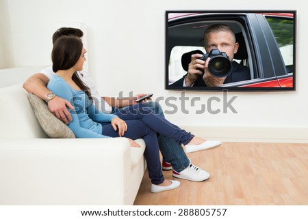 Young Couple In Livingroom Sitting On Couch Watching Television