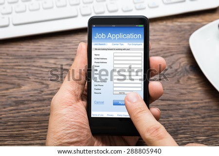 Close-up Of Person Hands Filling Online Job Application On Mobile Phone At Desk