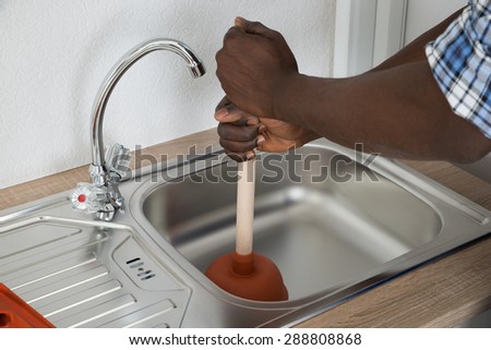 Close-up Of African Male Plumber Cleaning Sink With Plunger