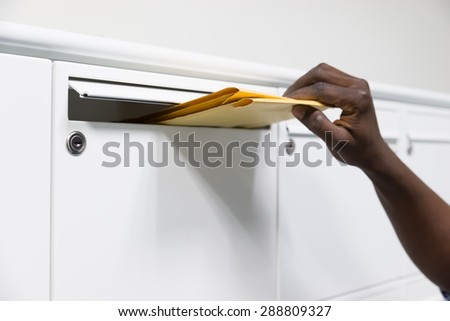 Close-up Of Person Hands Putting Envelope In Postbox