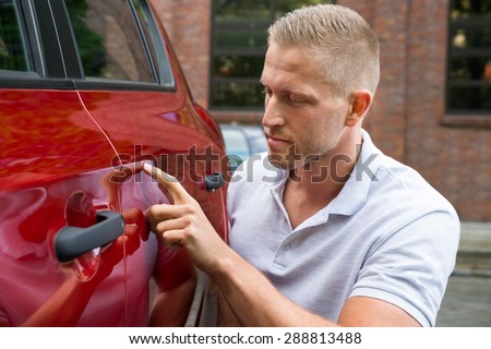 Close-up Of A Young Man Looking For Scratches On His Red Car