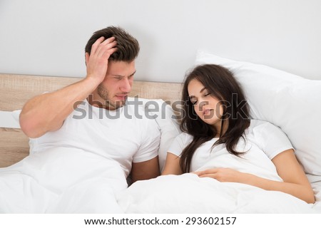 Upset Young Man Looking At Woman Snoring In Bed At Home