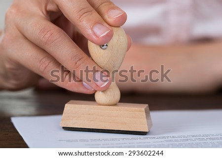 Close-up Of Person Hands Stamping Document At Desk