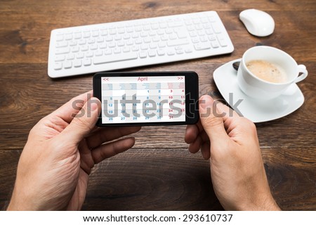 Close-up Of Person Hands With Mobile Phone Showing Calendar At Desk