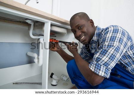 Close-up Of Happy African Male Plumber Fixing Pipe Of Sink In Kitchen