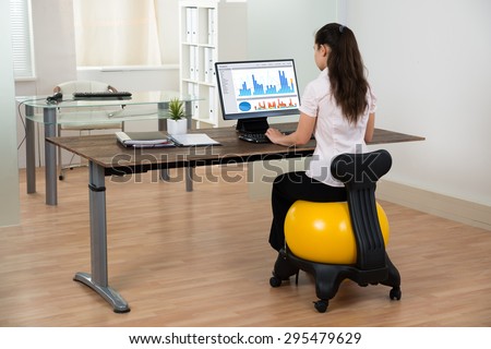 Young Businesswoman Sitting On Fitness Ball While Working On Computer In Office