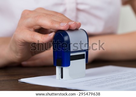 Close-up Of Person Hands Stamping Document At Desk