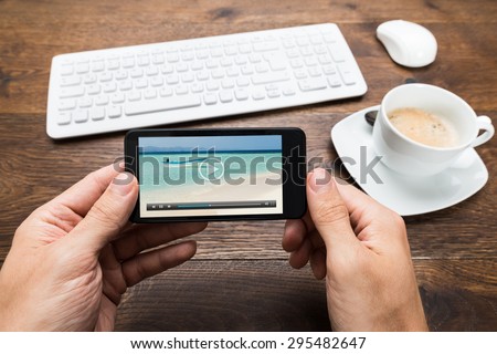 Close-up Of Person Watching Video On Mobile Phone With Cup Of Tea At Desk