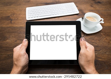 Close-up Of Person Hand Holding Digital Tablet With Keyboard And Tea Cup On Wooden Desk