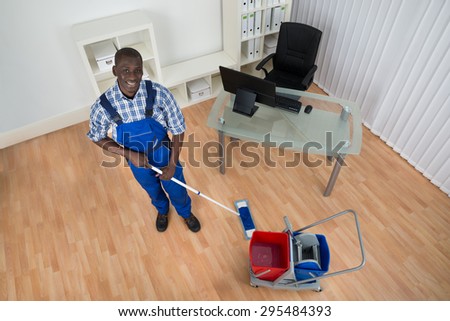 Young Happy Janitor Cleaning Floor With Wet Floor Sign