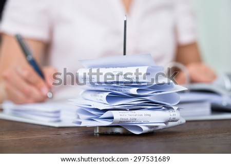 Close-up Of Bills In Paper Nail With Businessperson Working At Desk In Office