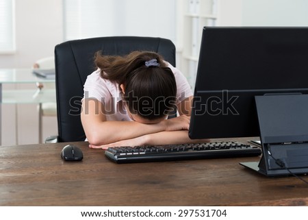 Young Businesswoman Sleeping On Desk In Front Of Computer In Office