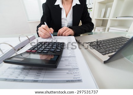 Close-up Of Businesswoman Calculating Invoice With Calculator