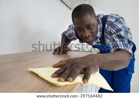 Young Happy Janitor Cleaning Kitchen Worktop With Rag And Cleaning Fluid