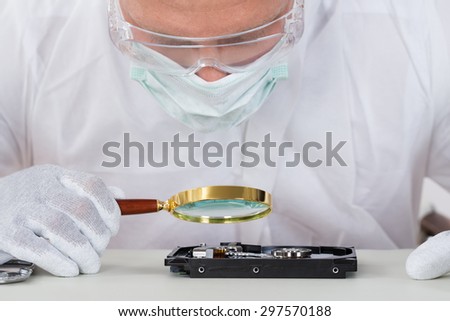 Close-up Of Young Man Looking At Harddisk With Magnifying Glass