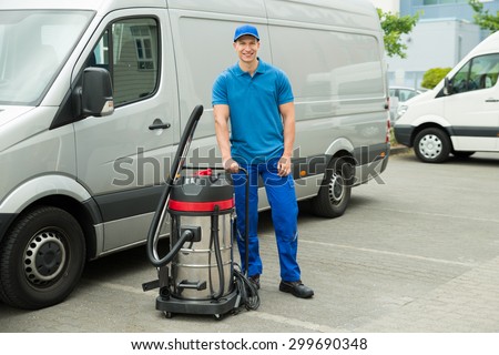 Happy Male Cleaner In Blue Uniform Standing With Vacuum Cleaner