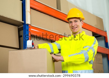 Male Worker Sealing Cardboard Box With Adhesive Tape In Warehouse