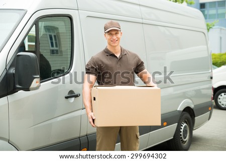 Happy Delivery Man Holding Box In Front Van