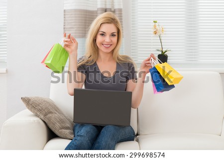 Young Happy Woman Sitting On Sofa With Laptop And Small Colorful Shopping Bags