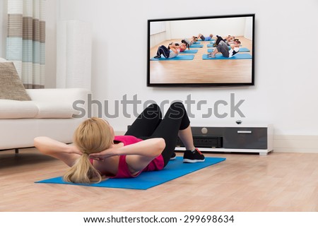 Young Woman Exercising On Blue Mat While Watching Television In House