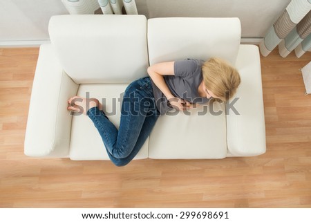 Young Woman On Sofa Suffering From Stomachache