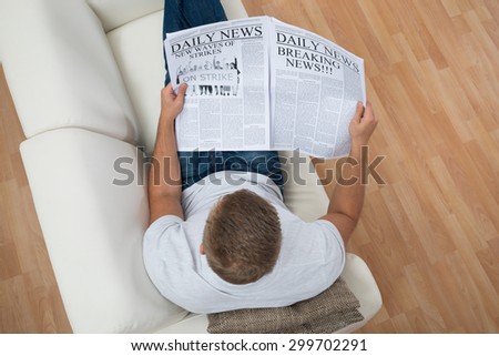 High Angle View Of Man Reading Newspaper On Sofa At Home