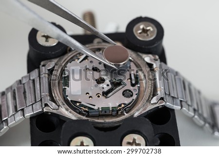 Close-up Of Tweezers Placing Battery On Silver Wrist Watch