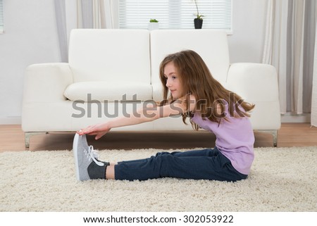 Cute Girl Exercising In Front Of Sofa On Carpet In Living Room