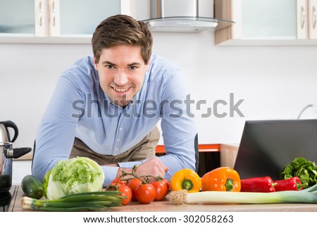Happy Man Leaning On Kitchen Counter With Laptop And Vegetables In Kitchen