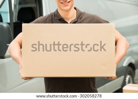 Close-up Of Young Delivery Man Carrying Box In Hand