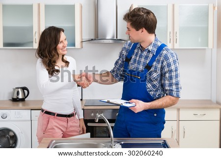 Young Woman Shaking Hands To Male Plumber With Clipboard In Kitchen Room