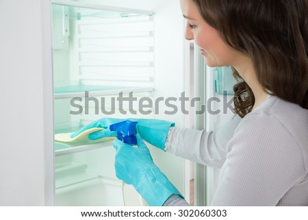 Close-up Of Happy Woman Cleaning Shelf Of Fridge With Rag