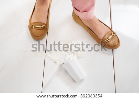 Close-up Of Female Leg Wearing Brown Footwear Standing Near The Yoghurt Spilled On Floor