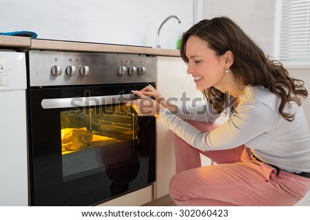 Happy Woman Roasting Chicken Meat In Kitchen Oven