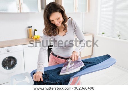 Happy Woman Ironing Trousers With Electric Iron At Home