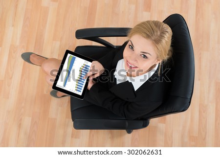 Happy Businesswoman Sitting On Office Chair With Digital Tablet Showing Graphs