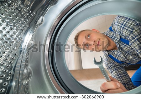 Young Repairman With Spanner Looking Inside The Washing Machine
