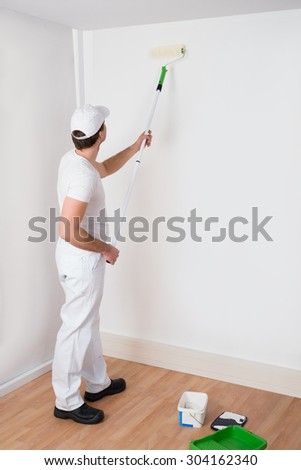 Young Painter In White Uniform Painting With Paint Roller On Wall
