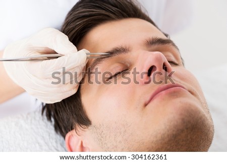 Close-up Of Beautician Hands Plucking Handsome Man Eyebrows With Tweezers