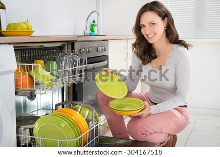 Young Happy Woman Arranging Plates In Dishwasher At Home