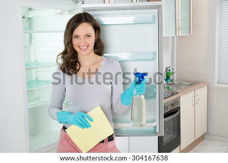 Young Beautiful Woman Standing With Rag And Spray Bottle Near The Open Fridge