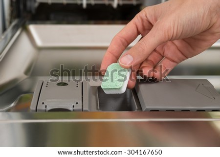 Close-up Of Person Hands Putting Dishwasher Soap Tablet In Detergent Dishwasher Box