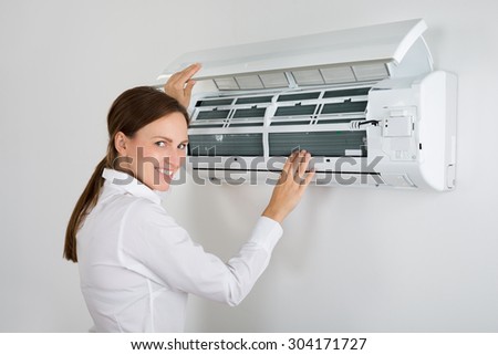 Young Businesswoman Checking Air Conditioner Mounted On Wall In Office