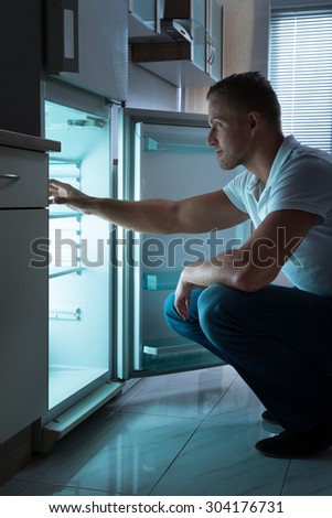 Young Man Sitting In Front Of Empty Fridge At Nighttime