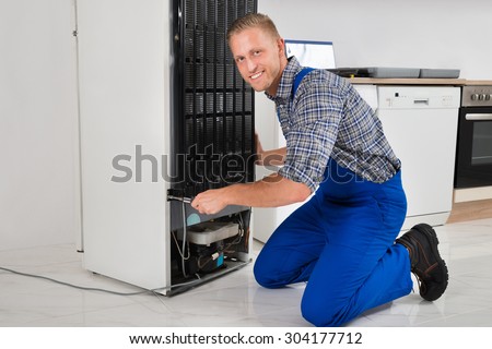 Male Worker Repairing Refrigerator With Screwdriver In House